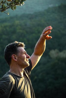 gegenlicht-natur.png Ein Mann im Profil blickt lächelnd nach oben und streckt seine Hand in Richtung des Sonnenlichts.