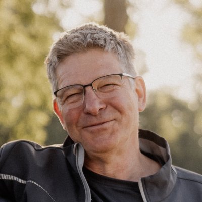 Anton_und_Gottfried_Bellin Zwei Männer stehen draußen im Park, lächeln in die Kamera und haben den Arm um die Schultern des jeweils anderen.