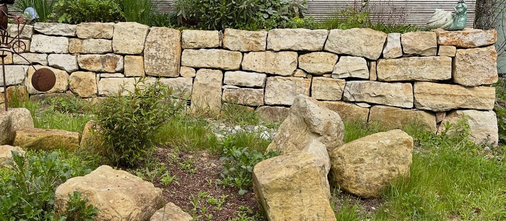 Natursteinmauer mit großen Findlingen und grüner Bepflanzung im Garten.